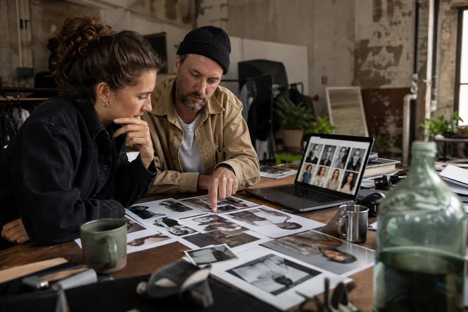 Brand producers choosing models from printed comp cards and a laptop grid